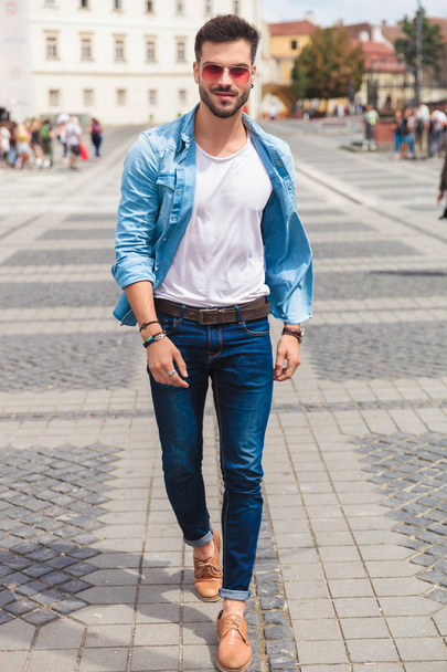 sexy casual man wearing red sunglasses walking on city streets and smiling, full length picture - Foto, Imagen
