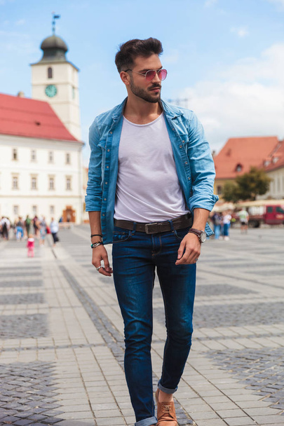 young casual man stepping forward on city streets looks down to side, full length picture - Foto, immagini