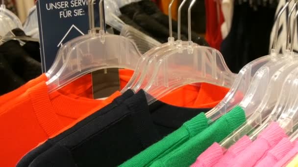 Stijlvolle kleren opknoping in rij op hangers in een kledingwinkel in een winkelcentrum. De inscriptie op het etiket van de dienst in Duits - Video