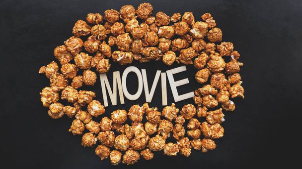 Golden caramel popcorn closeup. Background of popcorn. Wooden letters Movie - Фото, зображення