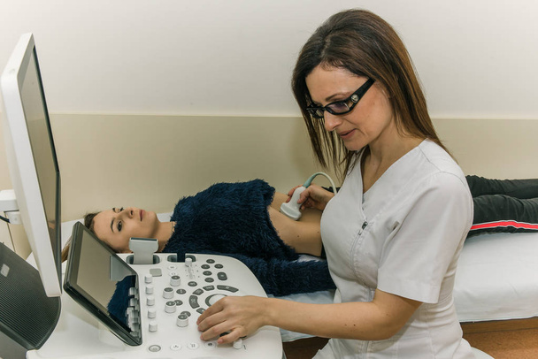 junge hübsche Ärztin führt eine Untersuchung der inneren Organe mit Hilfe eines Ultraschall-Mädchens durch - Foto, Bild