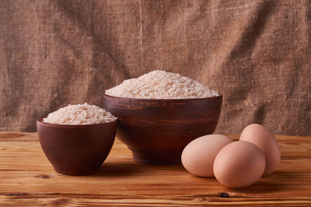 White rice in clay bowl on table and eggs on wood background - Photo, Image