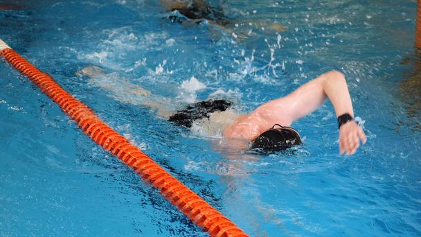 Close up for professional swimmer in slow mothion while swimming race in indoor pool. Athlete training, swimming the crawl in the pool. - Photo, Image
