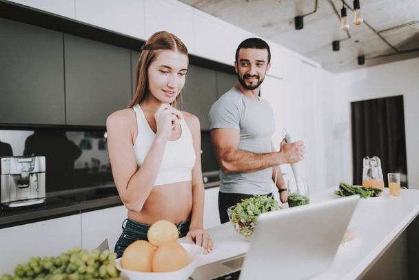 A Couple Is Preparing A Salad For A Breakfast. Cooking Together.. Healthy Lifestyle. Young And Handsome. Sport Body. Stare On Laptop. Dish Chopping. Morning Fresh Nutrition Concept. - Foto, Imagen