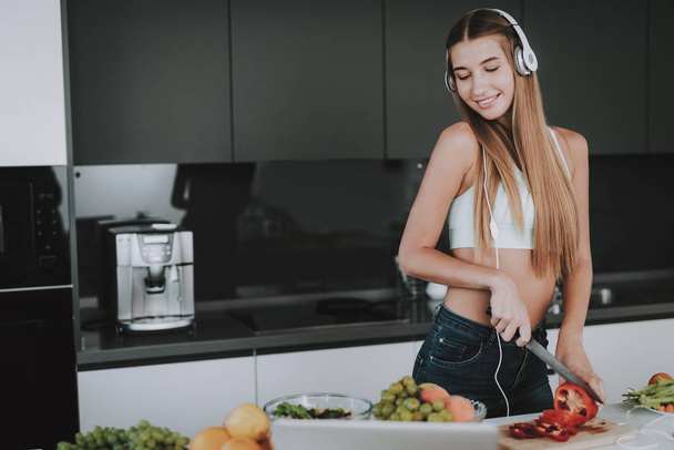 Girl Is Cooking And Listen To Music In Headphones. Healthy Lifestyle. Young And Handsome. Sport Body. House Interior. Fruits And Vegetables. Morning Fresh Nutrition. Role Model. Vitamons On Table. - Foto, Imagen
