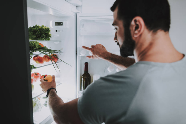 A Sporty Man Takes Vegetables From The Fridge. Kitchen Concept. Young And Handsome. Sport Body. House Interior. Open The Door. Morning Fresh Nutrition. Vitamins Recieving. Healthy Lifestyle. - Zdjęcie, obraz