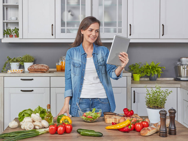 Giovane donna allegra che cucina in cucina con un tablet digitale
 - Foto, immagini