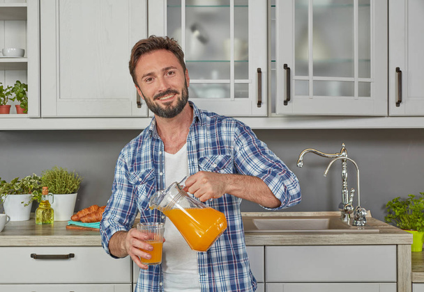 Hombre sano vertiendo jugo de naranja en la cocina
 - Foto, Imagen