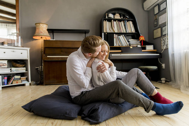 Feliz y cariñosa pareja joven sentada en el suelo de la habitación
 - Foto, Imagen