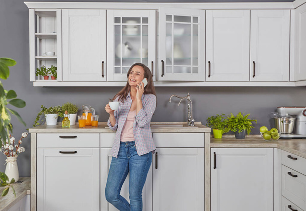 Young woman talking on mobile phone  in the kitchen - Photo, Image