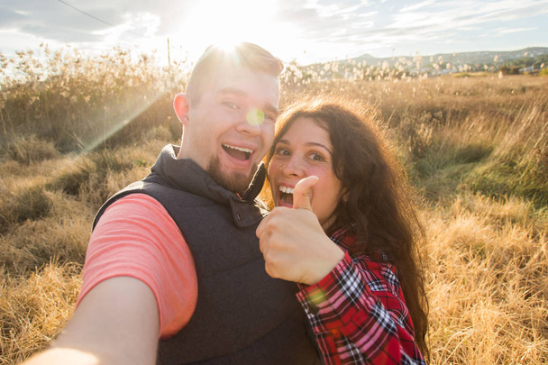 Travel, tourism and nature concept - Smiling couple taking selfie on field and showing thumbs up - Photo, Image