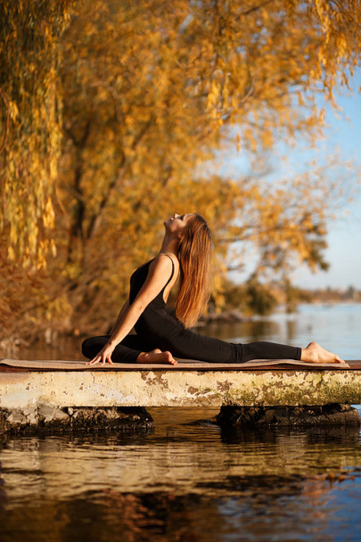 Young woman practicing yoga exercise at quiet pier in autumn park. - Fotografie, Obrázek