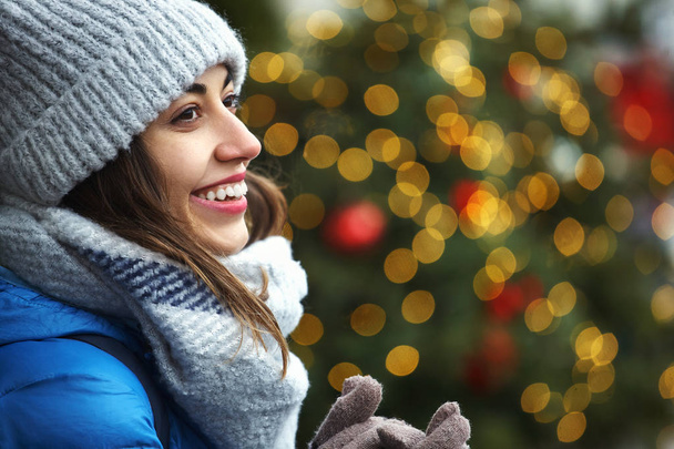 closeup horizontal image of a s happy smiling woman in warm winter clothes against the background of bright Christmas lights - Photo, Image