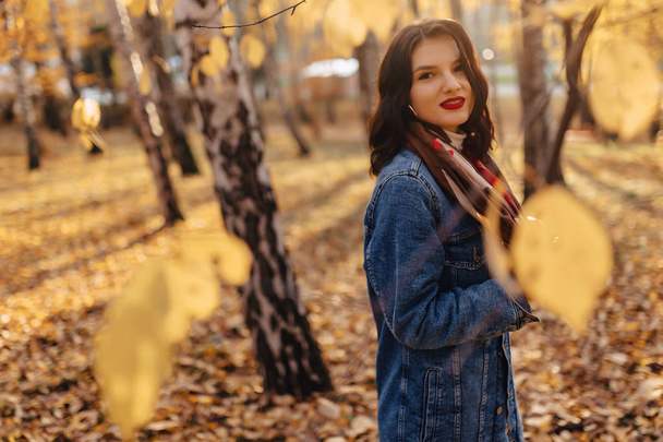 молода красива дівчина в джинсовому пальто гуляє в осінньому сонячному парку
 - Фото, зображення