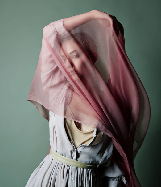 A beautiful young tender girl in a chiffon dress is covered with a drapery made of thin fabric that develops in the wind. - Photo, image