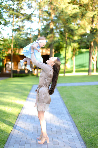 Fiatal, boldog nő viselt ruha gazdaság kis baba, kertben. - Fotó, kép