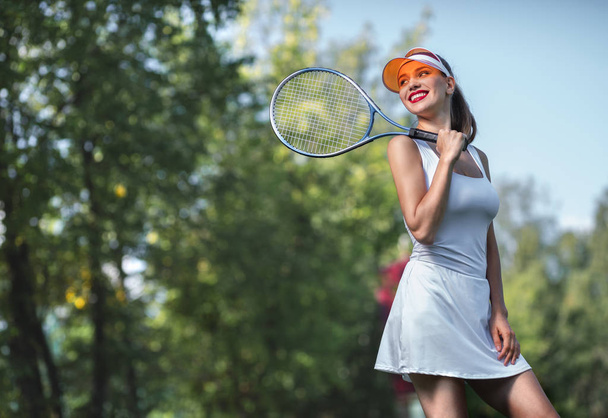 Улыбающаяся привлекательная девушка с теннисной ракеткой на открытом воздухе
 - Фото, изображение