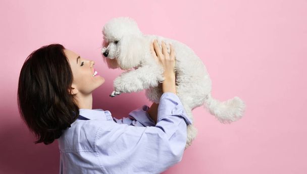 Beautiful woman hugging her lovely white poodle dog puppy on pink happy smiling - Zdjęcie, obraz