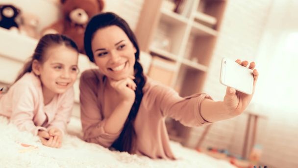 Fun with Daughter. Rest at Home. Child Development. Smiling Mom and Daughter. Happy Person in Pajamas. Girl and Mom Lie on Carpet. Colour Pencils. Smiling Mom and Daughter. Make Selfie. Phone in Hand. - Foto, Imagem