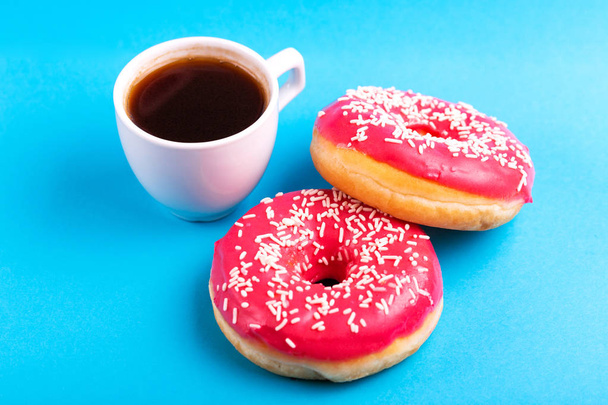 Two delicious pink donuts with sprinkle and cup of coffee on bright blue background. Unhealthy, but tasty sweets. Copy space. Top view - Fotografie, Obrázek