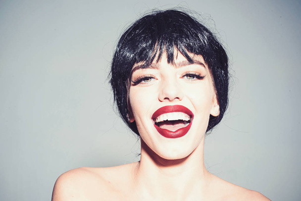 Girl on happy smiling face posing with naked shoulders. Lady in black wig with make up on grey background. Beautiful smile concept. Woman with attractive red lips looks at camera. - 写真・画像