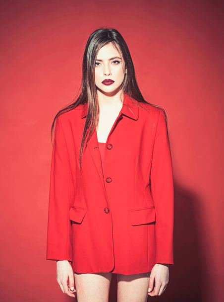 Fashion concept. Lady with dark lips looking at camera. Girl on mysterious face in red formal jacket, red background. Woman with stylish makeup and long hair posing in total red outfit. - Photo, Image