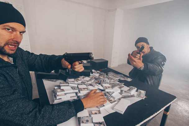 Dos criminales están sentados en una habitación oscura, hablando y contando dinero robado
 - Foto, Imagen