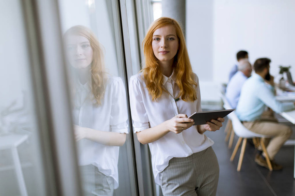 Dijital tablet modern ofis kullanan genç ve güzel kızıl saçlı kadın - Fotoğraf, Görsel