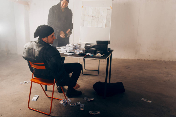 Dos criminales están sentados en una habitación oscura, hablando y contando dinero robado
 - Foto, Imagen