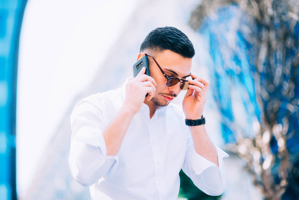 Κομψό επιχειρηματίας μιλάει στο κινητό του τηλέφωνο ενώ κοιτάζοντας το σημειωματάριό του. - Φωτογραφία, εικόνα