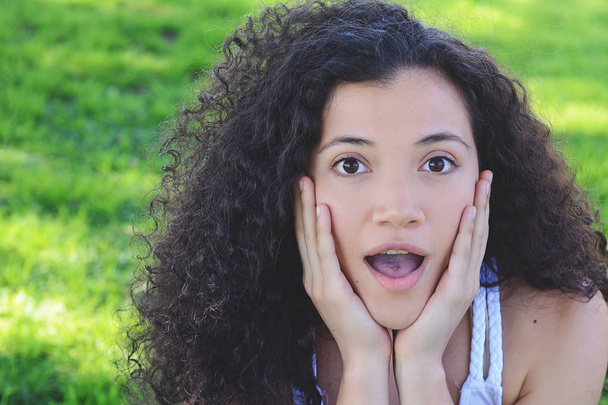 Outdoor portrait of a young beautiful latin woman with surprised facial expression on a summer park background. - Foto, Imagen