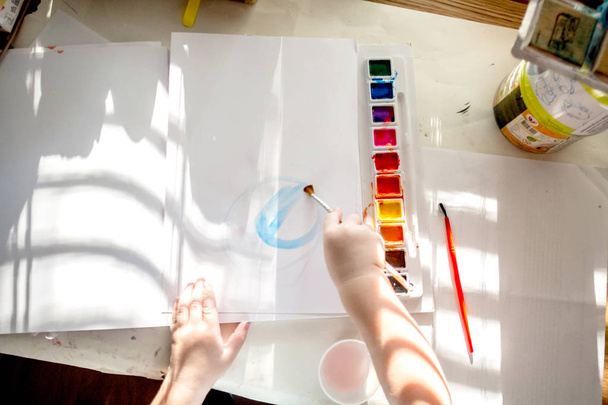 Мальчик веселится, играя с марками и темпера краски на деревянном рабочем столе с большим количеством грязных на руках и пальцах производства многоцветных творений
 - Фото, изображение