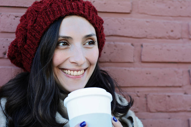 Retrato de una hermosa mujer sosteniendo una taza de café de papel en la calle. Escena urbana. Al aire libre
 - Foto, imagen
