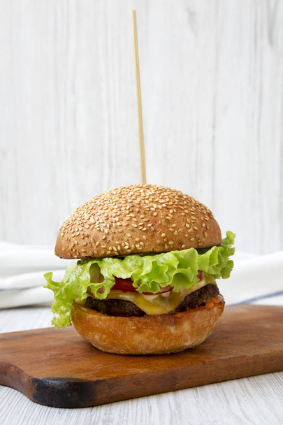 Homemade cheeseburger on wooden board over white wooden surface, side view. Close-up. - Photo, Image