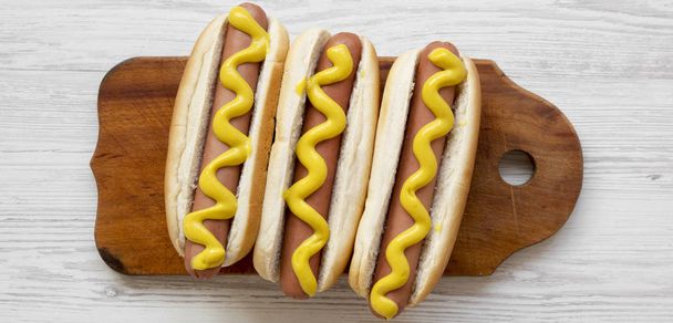 Hot dog with yellow mustard on wooden board on white wooden background, top view. Flat lay, overhead, from above. Closeup. - Foto, immagini