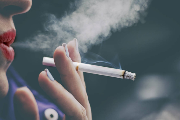 У девушки только губы выдыхают дым, держа сигарету в руке. мелкая глубина разреза. there is toning
. - Фото, изображение