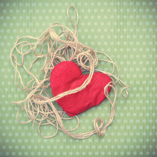 Coração vermelho envolto em fio vintage em fundo verde
 - Foto, Imagem