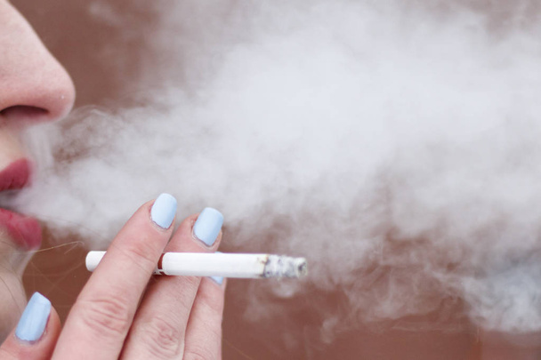 У девушки только губы выдыхают дым, держа сигарету в руке. мелкая глубина разреза. there is toning
. - Фото, изображение