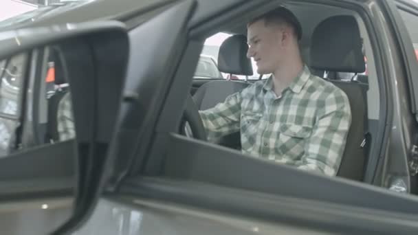 Facet siedzi na siedzeniu kierowcy. Szczęśliwy młody człowiek pewny siebie na światła we wnętrzu, sprawdza, czy salon samochodowy - Materiał filmowy, wideo