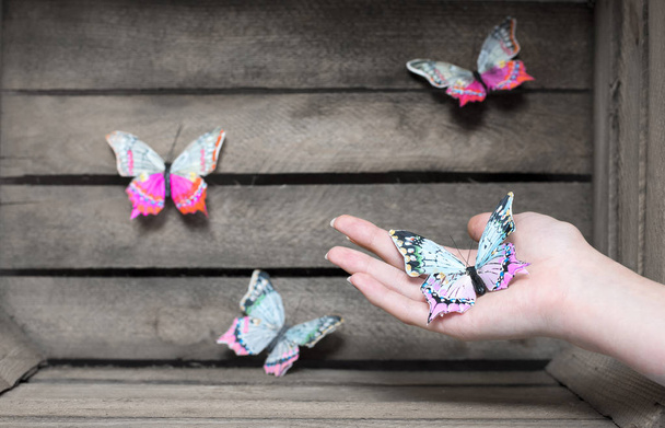 Una mariposa colorida decorativa en una mano con mariposas de árbol en el fondo
 - Foto, Imagen