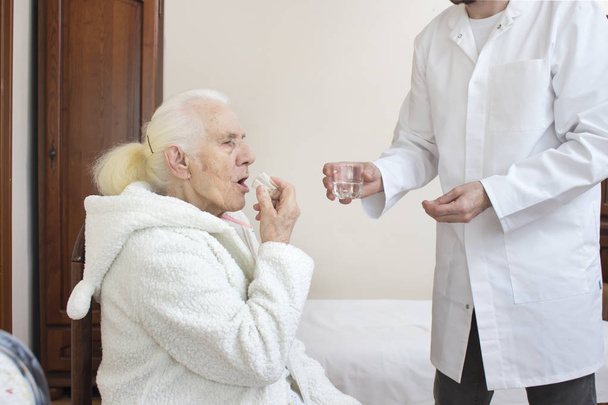The male nurse gives a glass of water to the old woman during medication. - Photo, Image