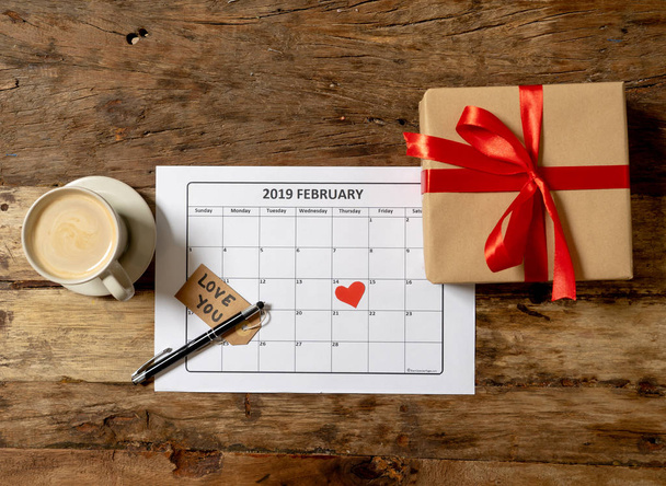 Top view of red heart on the 14 th of february 2019 calendar and present gift wrapped with love you message on vintage table in ready for saint Valentines day date and romantic celebration concept. - Photo, image