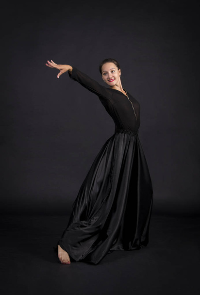 A young,smiling girl in black suit dancing modern choreography.Studio shot on dark background, isolated image. - Foto, afbeelding