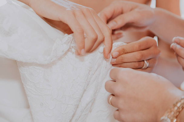 Bride getting ready to get married. Bride's hands with ring unbuttoning white wedding dress with other helping hands - Photo, Image
