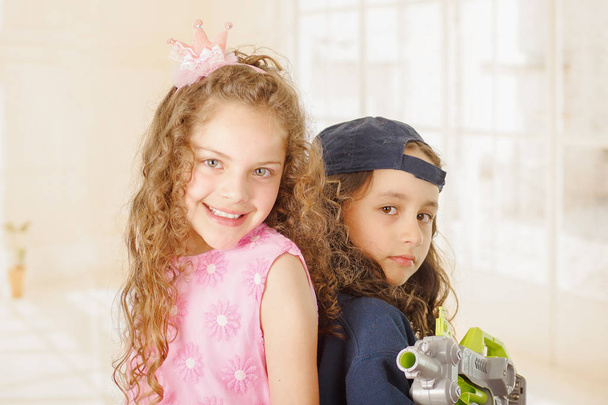 Close up of two girls one is wering boy clothes and holding a gun and other girl is wearing a pink princess dress - Foto, immagini