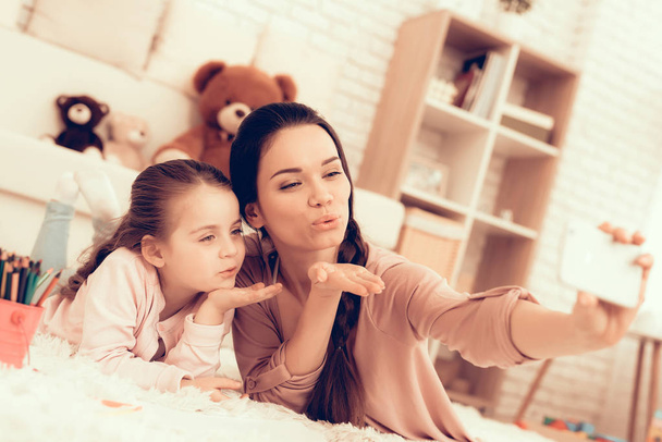 Make Kiss for Selfie. Rest at Home. Child Development. Mom and Daughter. Happy Person in Pajamas. Girl and Mother Lie on Carpet. Colour Pencils. Smiling Mom and Daughter. Make Selfie. Phone in Hand. - Foto, Bild