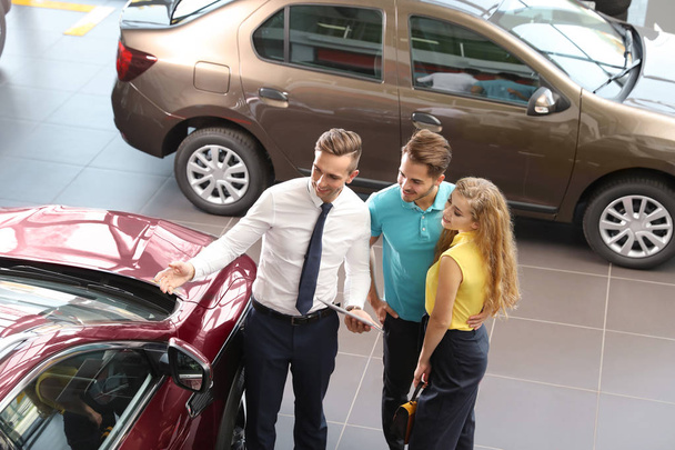 Young car salesman working with clients in dealership - Foto, Imagen