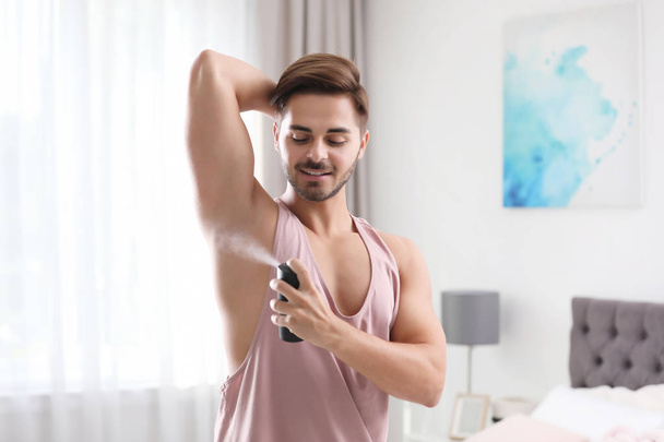 Handsome young man applying deodorant in room - Valokuva, kuva