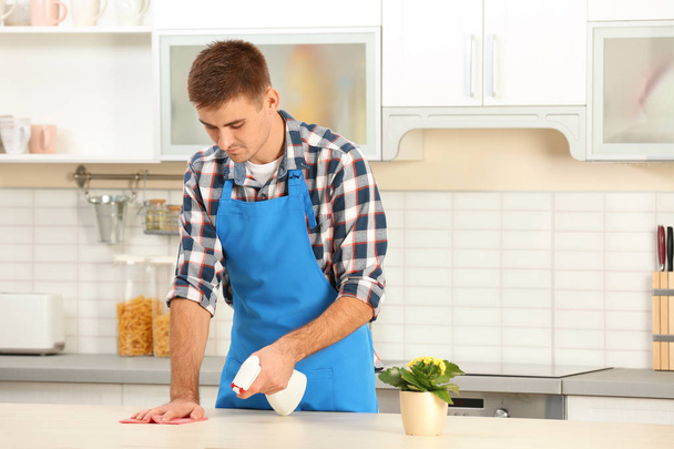 Male janitor cleaning kitchen furniture with rag in house - Foto, Imagen