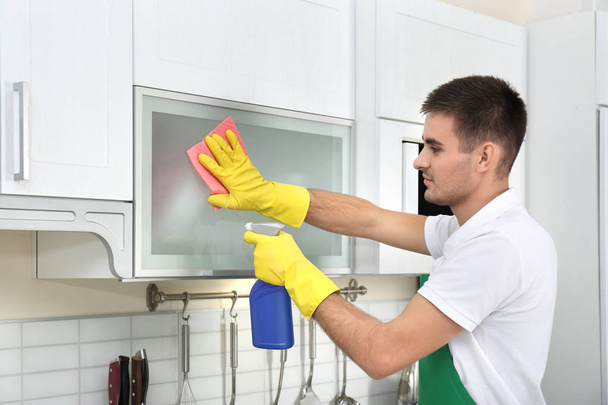 Male janitor cleaning kitchen furniture with rag in house - Foto, immagini